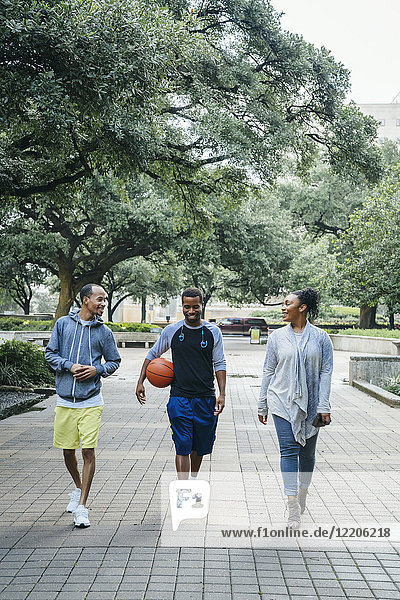 Lächelnde schwarze Freunde gehen im Park mit Basketball