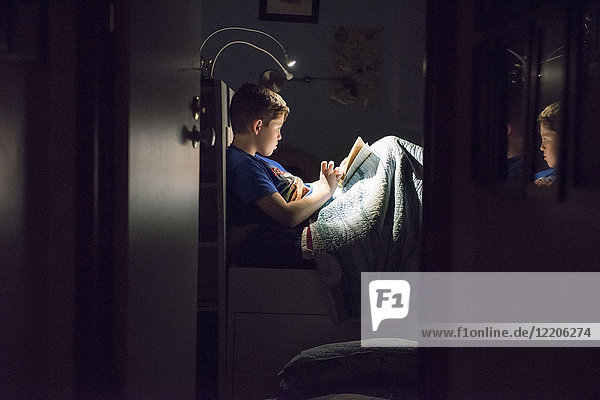 Kaukasischer Junge liest nachts im Bett ein Buch