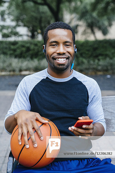 Porträt eines schwarzen Mannes  der Ohrstöpsel hört und einen Basketball hält