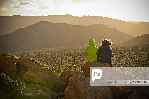 Jungen sitzen auf einem Felsen und bewundern die Wüstenlandschaft