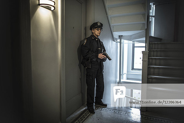 Ältere kaukasische Polizistin mit Waffe im Treppenhaus einer Wohnung