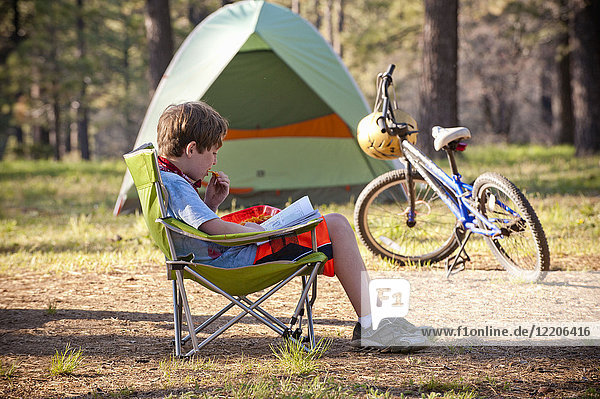 Kaukasischer Junge  der auf einem Campingplatz ein Buch liest