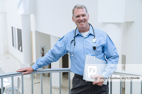 Portrait of smiling Caucasian doctor leaning on railing holding laptop