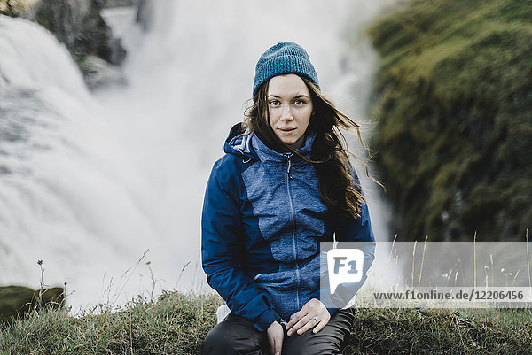 Porträt einer ernsten kaukasischen Frau  die in der Nähe eines Wasserfalls sitzt