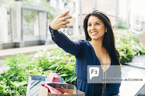 Hispanische Frau  die auf einer Bank sitzt und für ein Selfie mit ihrem Handy posiert