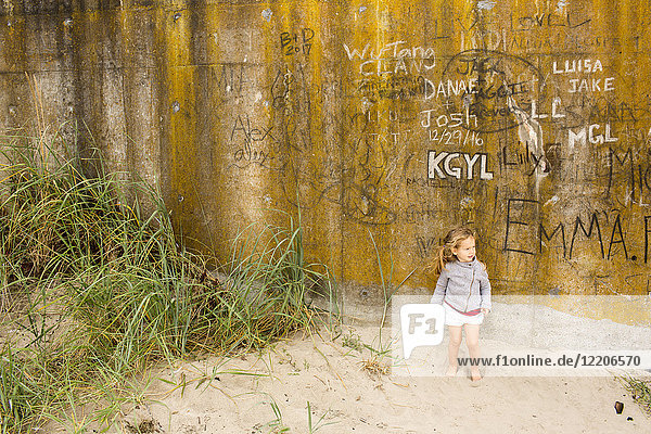 Kaukasisches Mädchen steht im Sand in der Nähe einer Graffiti-Wand