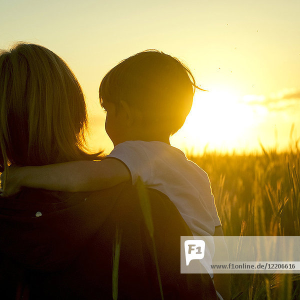 Mutter trägt Sohn in einem Weizenfeld bei Sonnenuntergang