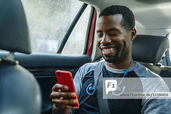 Lächelnder schwarzer Mann  der im Auto eine SMS auf seinem Handy schreibt