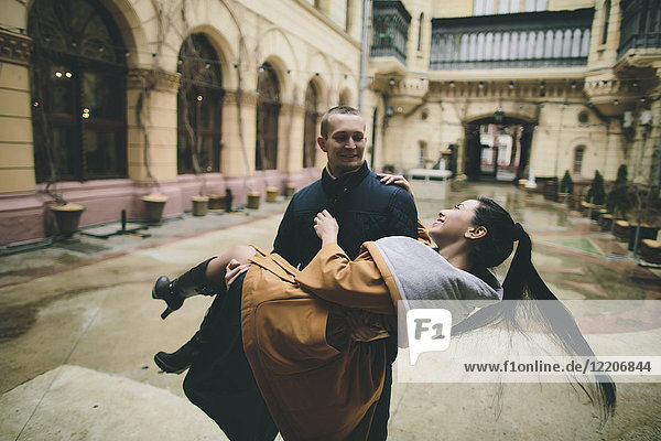 Caucasian man lifting and carrying woman in courtyard