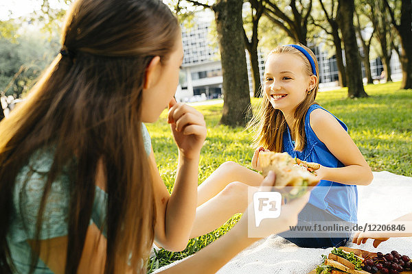 Smiling Caucasian sisters eating food at picnic