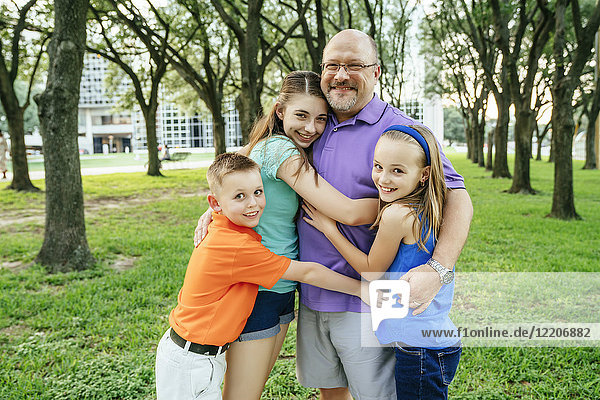 Portrait of Caucasian boy and girls hugging father in park