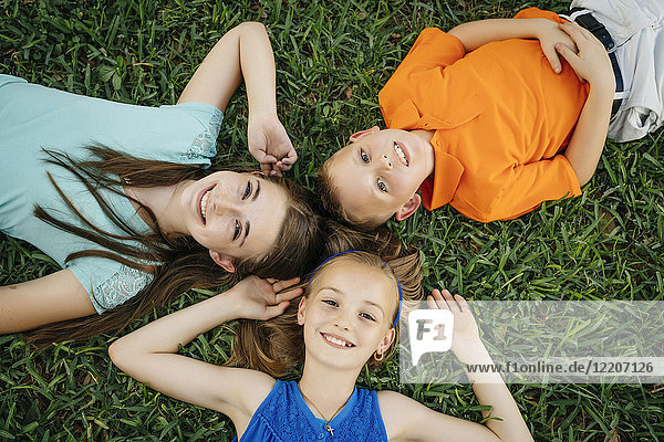 Close up portrait of smiling Caucasian brother and sisters laying on grass