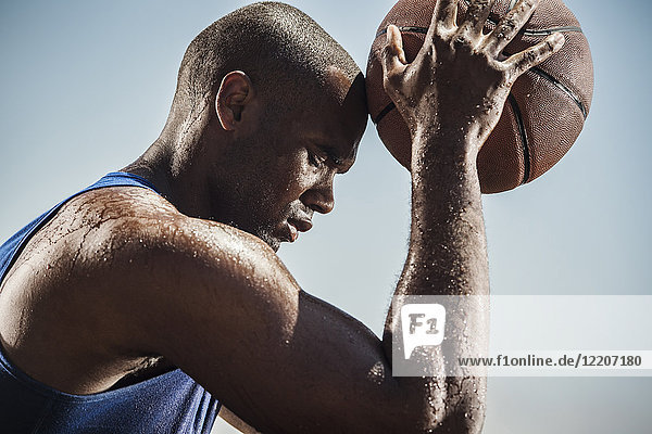 Portrait of sweating Black man touching forehead with basketball