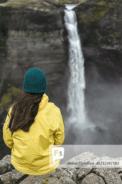 Caucasian woman sitting on cliff admiring waterfall