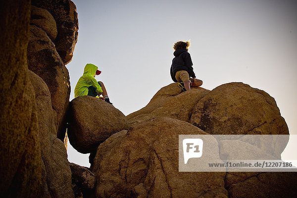 Boys sitting on rocks under blue sky