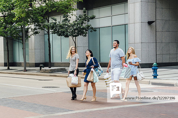 Friends crossing street in city carrying shopping bags