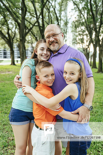 Portrait of Caucasian boy and girls hugging father in park