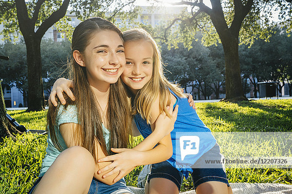 Portrait of smiling Caucasian sisters hugging in park