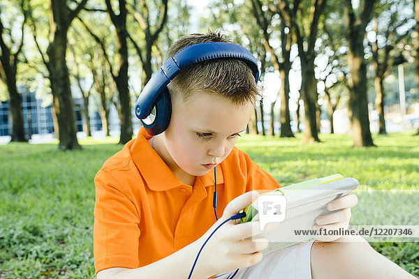 Serious Caucasian boy listening to digital tablet in park