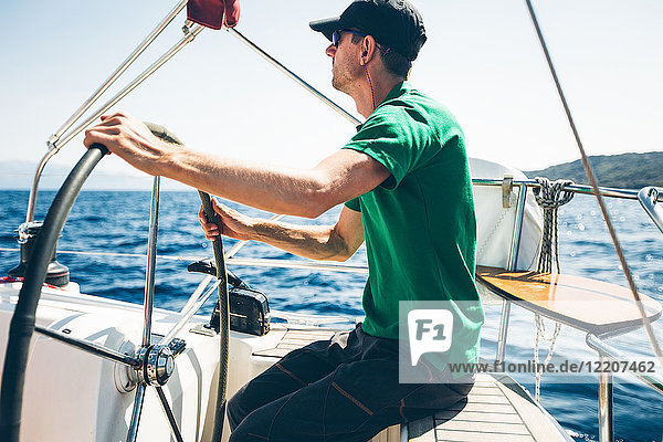 Mittelgroßer Mann steuert Yacht in Küstennähe  Kroatien
