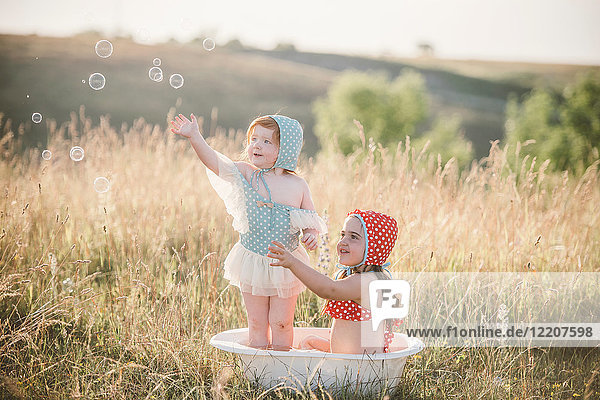 Two girls in field  playing in plastic tub of water