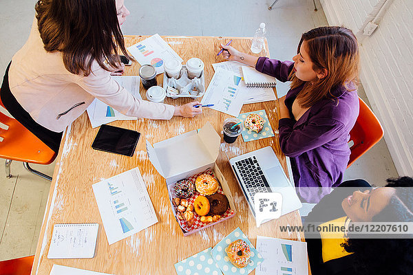 Kollegen arbeiten am Schreibtisch zusammen und teilen sich Doughnuts