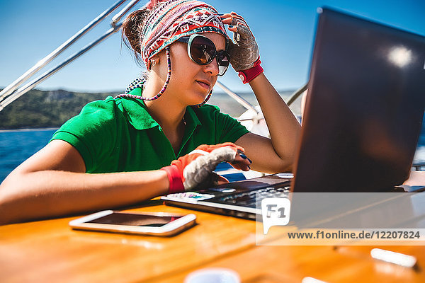 Junge Frau betrachtet Laptop an Bord einer Yacht in Küstennähe  Kroatien