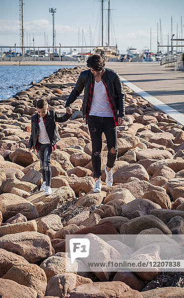 Father and son walking on rocks beside sea