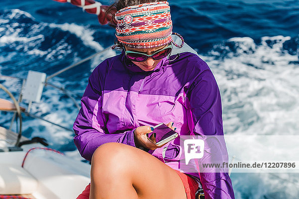 Junge Frau betrachtet Smartphone an Bord einer Yacht  Kroatien