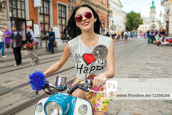 Porträt einer jungen Frau mit rosa Sonnenbrille auf einem Roller auf einer gepflasterten Straße  Odessa  Ukraine