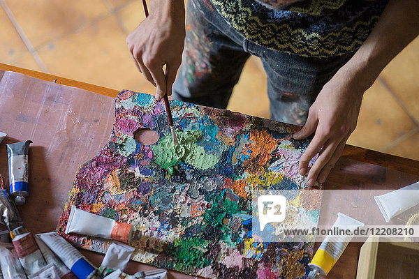 Männlicher Künstler beim Mischen von Ölfarbe auf der Palette im Künstleratelier  mittlerer Abschnitt