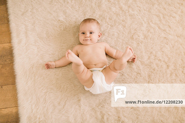 Overhead portrait of cute baby girl in diaper lying on beige rug