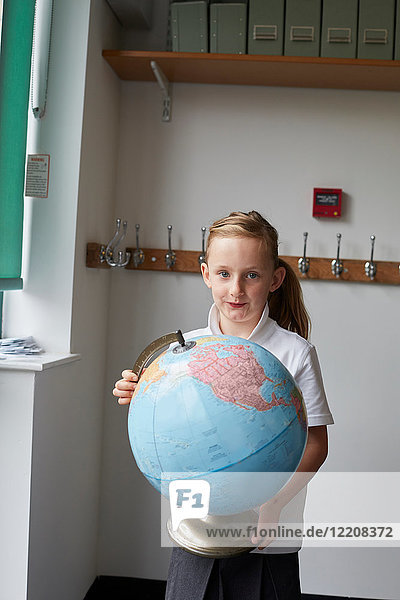 Schulmädchen hält Globus im Klassenzimmer der Grundschule  Porträt