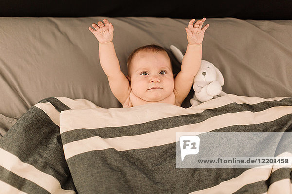 Portrait of baby girl lying in bed with arms raised  overhead view