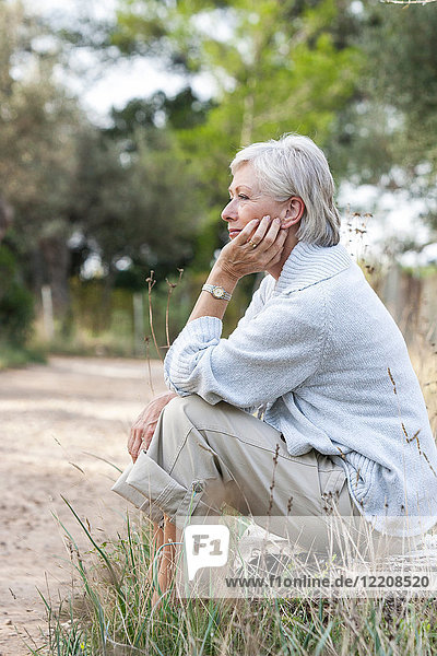 Ältere Frau sitzt in ländlicher Umgebung  nachdenklicher Ausdruck