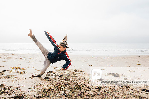Young boy on beach practising martial arts leg raised in kick