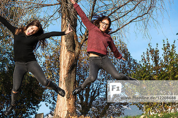 Zwei junge Frauen springen mitten in der Luft in einem Waldgebiet  Calolziocorte  Lombardei  Italien