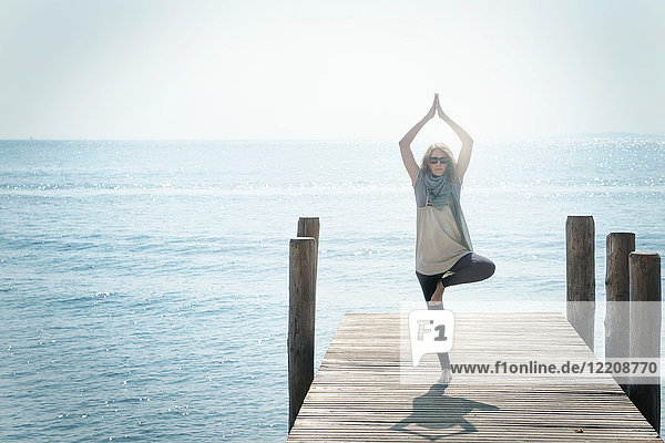 Frau auf dem Pier beim Balancieren auf einem Bein in Yoga-Pose
