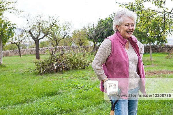 Ältere Frau im Garten  lehnt sich an Gartengerät an