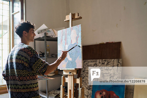 Männlicher Künstler malt Leinwand an der Staffelei im Künstleratelier