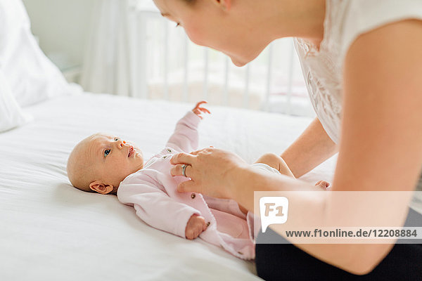 Young woman dressing baby daughter on bed
