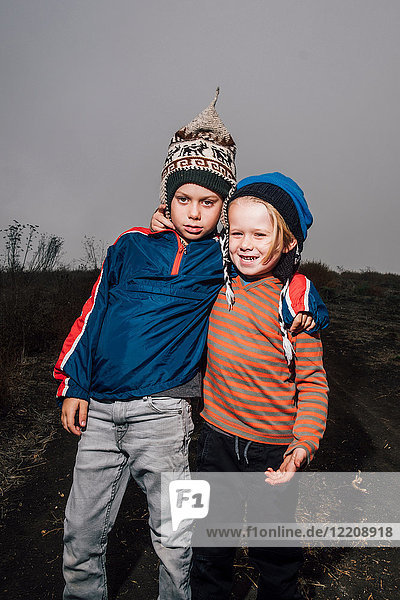 Portrait of two brothers outdoors wearing knitted hats arms around each other