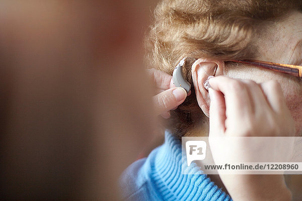 Reife Frau hilft älterer Frau beim Einsetzen des Hörgeräts  Nahaufnahme  differenzierter Fokus