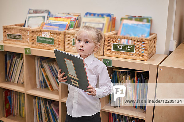 Süßes Schulmädchen hält Buch im Klassenzimmer der Grundschule