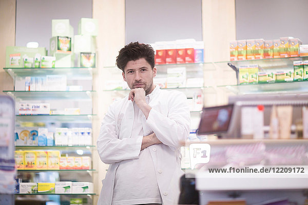 Porträt eines jungen männlichen Apothekers mit Hand am Kinn in der Apotheke