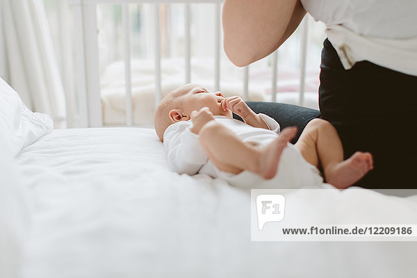 Young woman sitting on bed with baby daughter  cropped