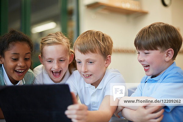 Schoolboys and girls laughing at digital tablet in classroom at primary school