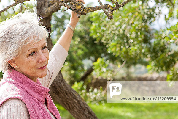 Porträt einer älteren Frau im Garten  die einen Baumzweig hält
