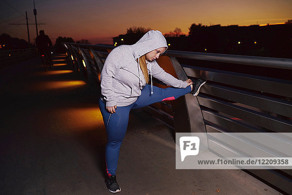 Kurvenreiche junge Frau trainiert  berührt nachts auf dem Steg die Zehen