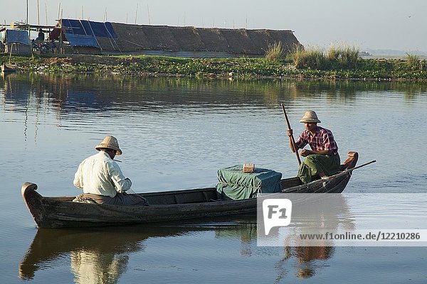 Local men fishing in canoe boat Sunrise over the lake near wooden foot bridge U Bein Bridge crossing the Taungthaman Lake near Amarapura in Mandalay Myanmar.